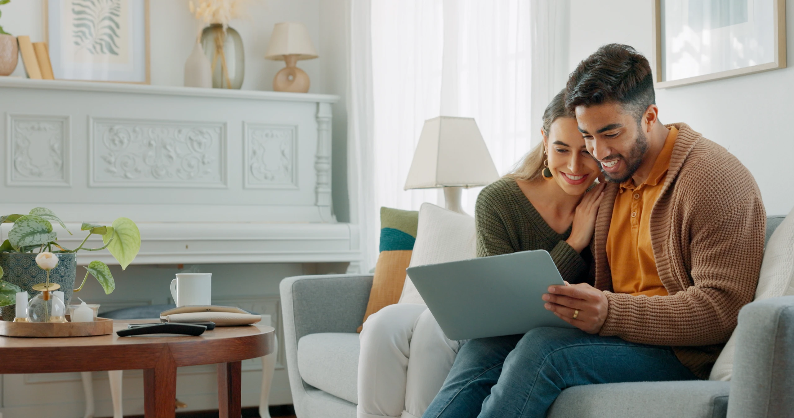 A man and woman couple sitting on their sofa together looking at a tablet.